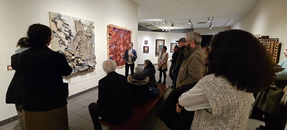 A crowd of people listens as an artist explains their piece in a gallery