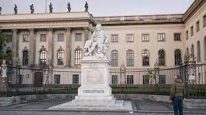 A statue sits in the middle of a square surrounded by buildings at Humbolt Universität zu Berlin