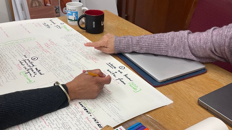 Two people working together on a poster board of written ideas.