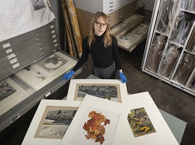 Deirdre Madeleine Smith stands at a table with archived artwork