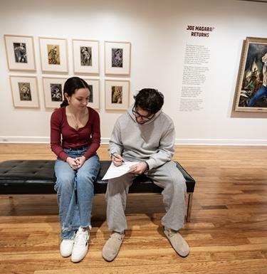 Students sit on a bench in the middle of an art gallery room