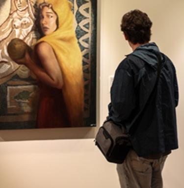 Student looks at painting hanging on gallery wall