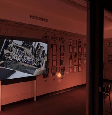 Art installation that features photographs hanging in a dimly lit room with a film playing on the tv.