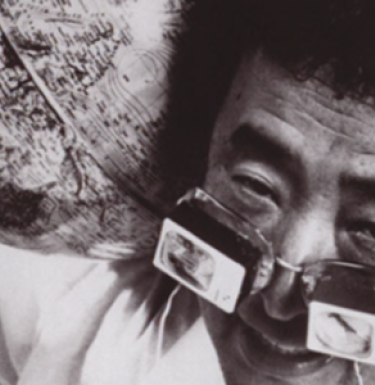 Black and white photo of artist Nam June Paik wearing special magnifying glasses