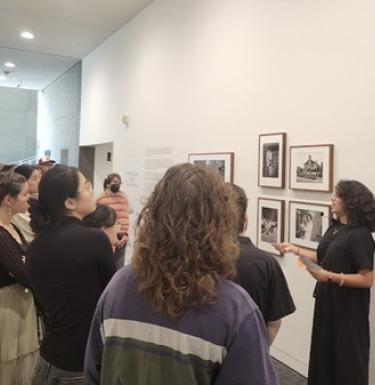 Professor Kale Serrato Doyen talks to a group of students in an art gallery